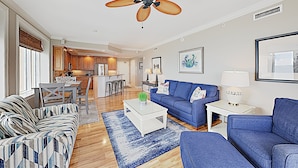 A spacious living room with a blue sofa, a patterned sofa, a coffee table, and a ceiling fan.
