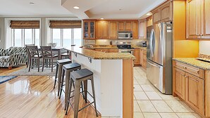 A modern kitchen with wooden cabinets, stainless steel appliances, and a bar area with stools.