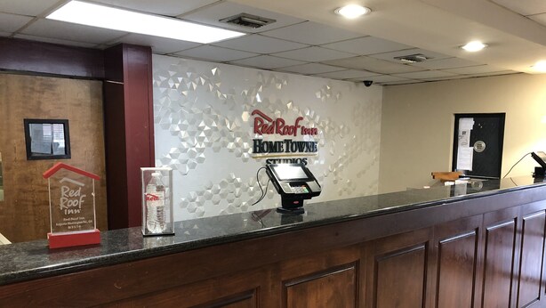 A hotel reception desk with a Red Roof Inn sign, a water bottle, and a payment terminal. - HomeTowne Studios By Red Roof Augusta (Augusta)