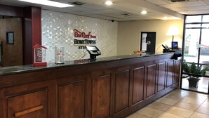 A reception desk with a Red Roof Inn sign, a cash register, and a small plant. - HomeTowne Studios By Red Roof Augusta (Augusta)
