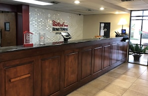 A reception desk with a Red Roof Inn sign, a cash register, and a small plant. - HomeTowne Studios By Red Roof Augusta (Augusta)