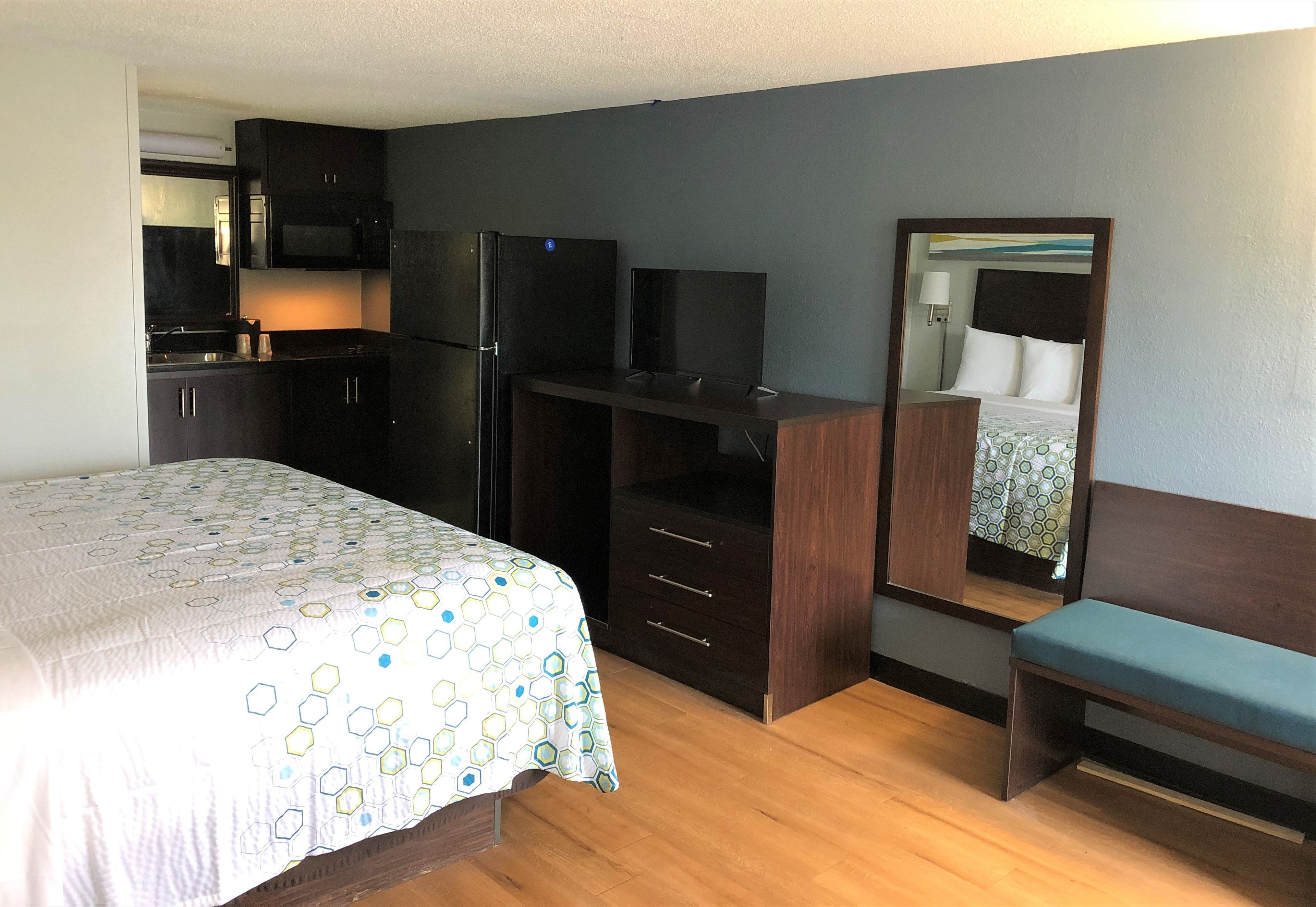 Une chambre d’hôtel équipée d’un lit, d’un bureau, d’un miroir, d’une télévision et d’une kitchenette.