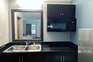 A compact kitchenette with a double sink, a microwave, and a refrigerator. - HomeTowne Studios By Red Roof Augusta (Augusta)
