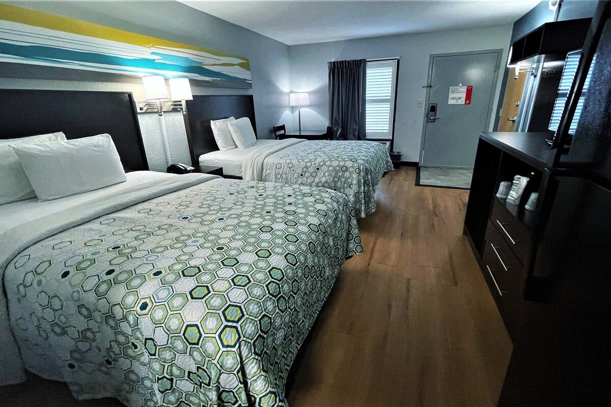 A hotel room with two beds, a desk, a chair, a TV, and a wardrobe.