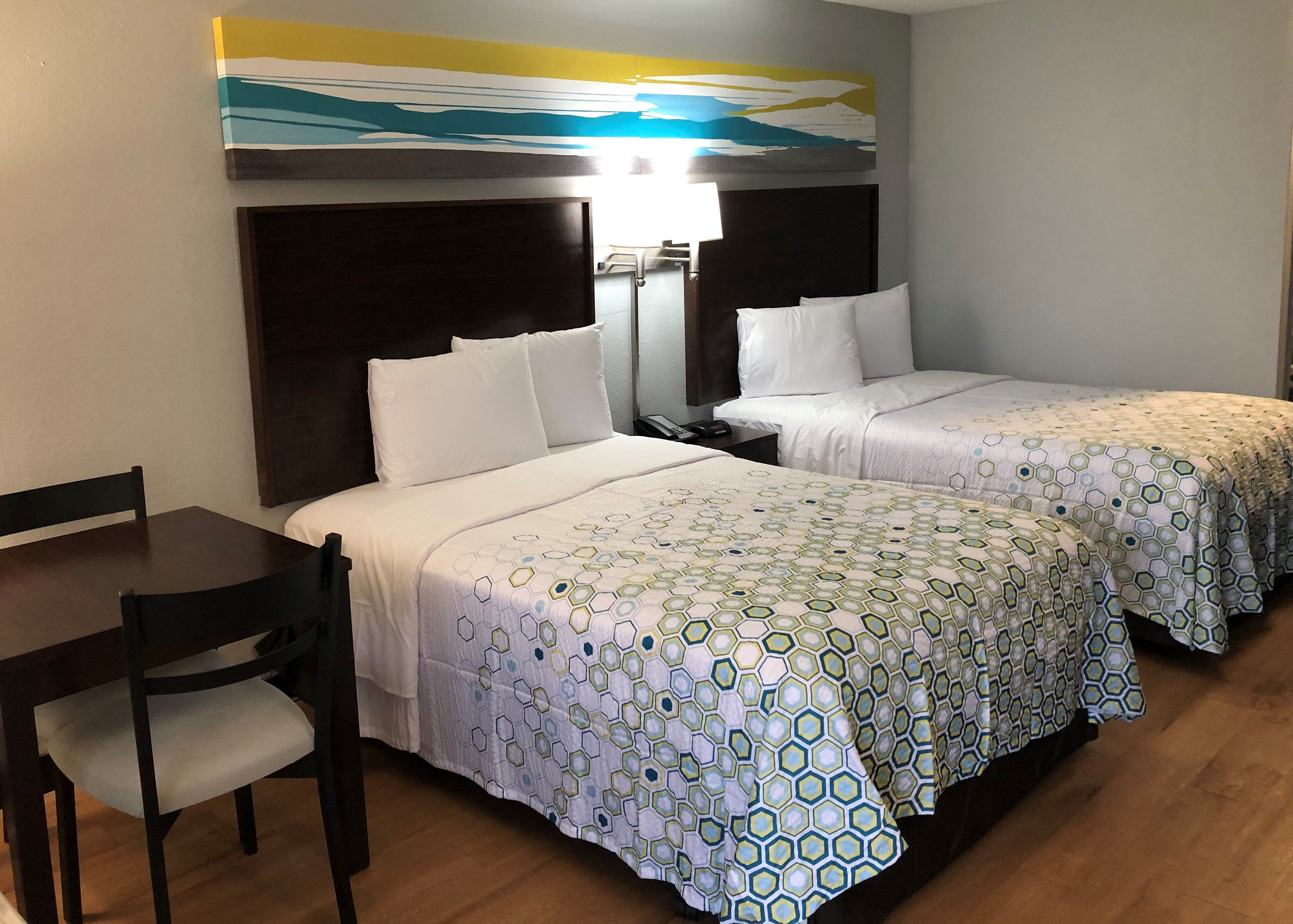 Quarto de hotel com duas camas, uma escrivaninha e uma cadeira.