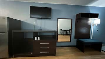 Una habitación compacta con kitchenette, un televisor de pantalla plana en la pared, un espejo grande que refleja un comedor y un banco.