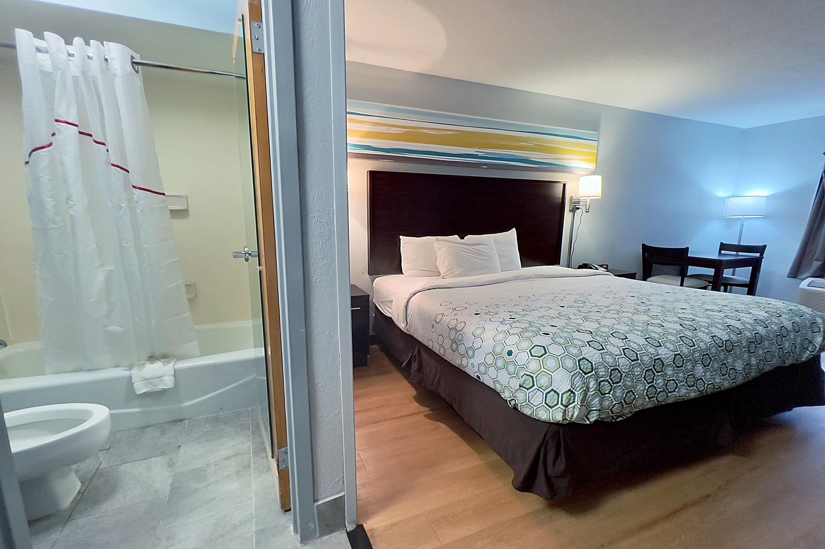 Une chambre d’hôtel équipée d’un lit, d’une douche, de toilettes et d’un bureau avec des chaises.