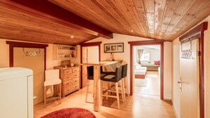 Ein gemütliches Zimmer mit Holzbalkendecke, einem Esstisch mit Stühlen, einem roten Teppich und einem weißen Schrank.