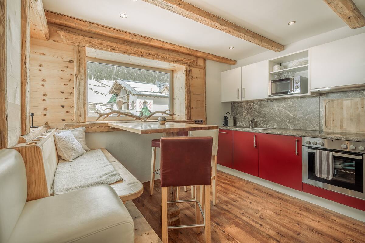 A cozy kitchen with wooden beams, a built-in stove, and a view of a snowy landscape.