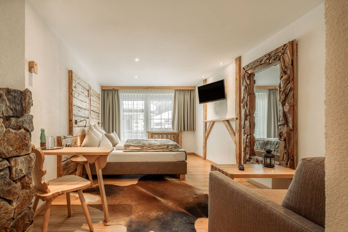 A bedroom with a bed, a TV, a stone wall, a wooden desk, and a large mirror.