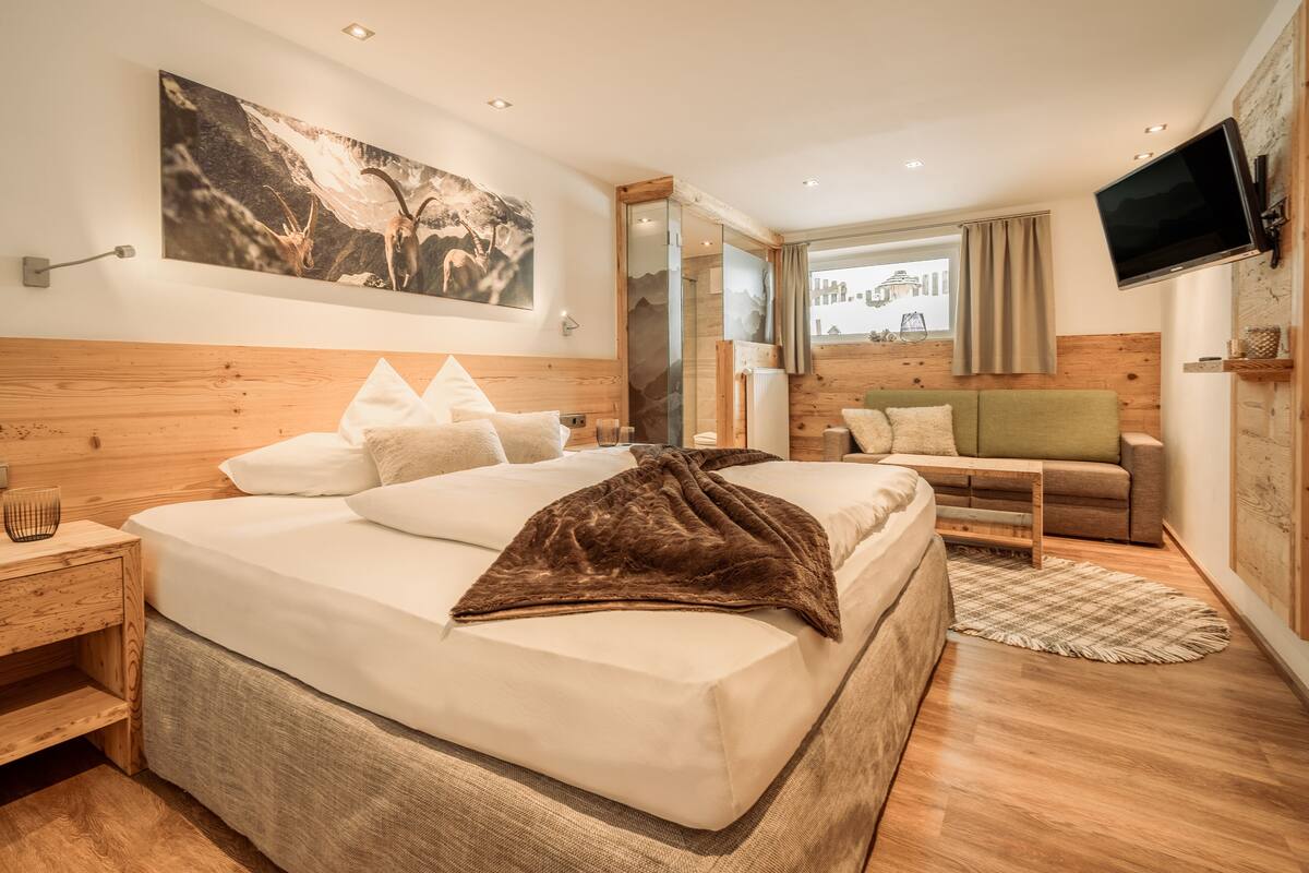 A modern bedroom with a large bed, a sofa, a TV, and a painting on the wall.