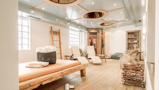 Ein Zimmer mit einem Holzbett, zwei Stühlen, einem kleinen Tisch und einem Holzstoß.