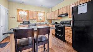 A kitchen with wooden cabinets, a black refrigerator, a microwave, and a stove. - 🐾5 Pleasant Street - Conveniently located in town, dog friendly (Rangeley)