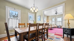 A dining area with a wooden table and chairs, a colorful rug, and a ceiling fan. - 🐾5 Pleasant Street - Conveniently located in town, dog friendly (Rangeley)