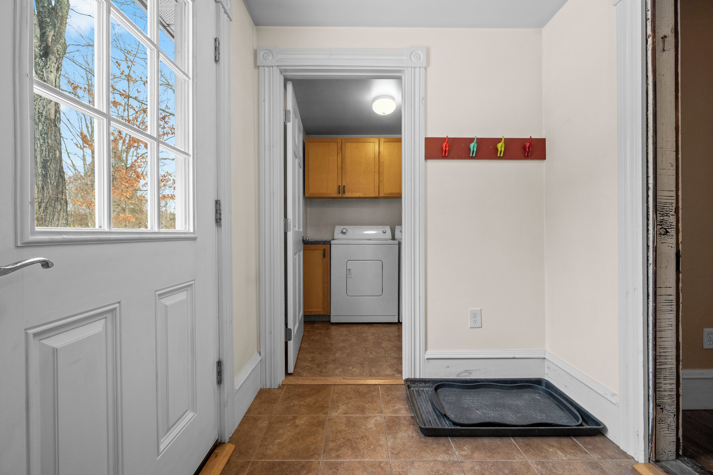 A hallway leading to a laundry area with a door, a window, and a wall-mounted shelf with figurines.