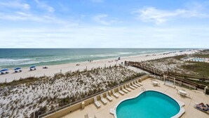 A beach view with a swimming pool, lounge chairs, and umbrellas.
