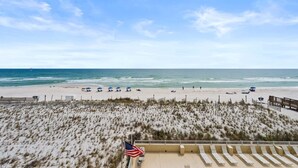 A beach view with a sandy area, a flag, and a wooden structure.