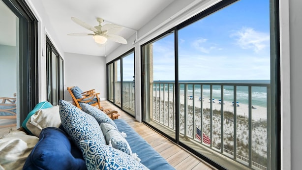 A balcony with a view of the beach, a ceiling fan, and a sofa with patterned cushions.