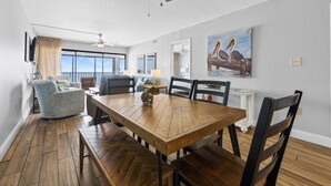 A dining area with a wooden table and chairs, a ceiling fan, and a view of the ocean through large windows.
