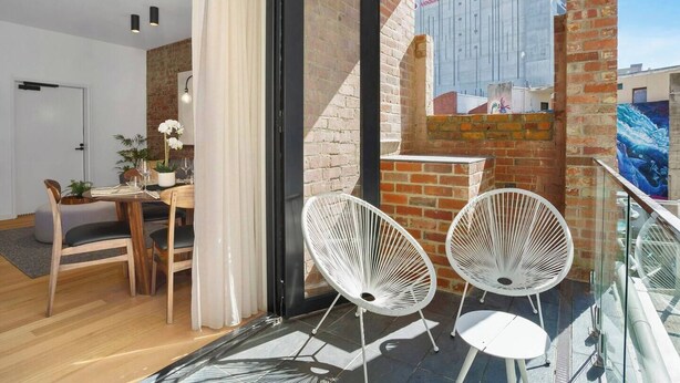 A modern apartment with a dining area, a balcony with white chairs, and a view of a building with a Vodafone advertisement.