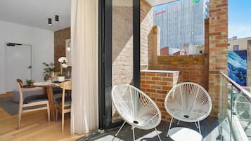 A modern apartment with a dining area, a balcony with white chairs, and a view of a building with a Vodafone advertisement.