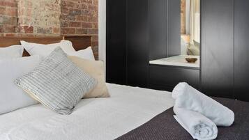 Une chambre d’hôtel avec un mur en briques, un lit avec du linge de maison blanc, une armoire en bois sombre et une petite table de chevet avec un bol.