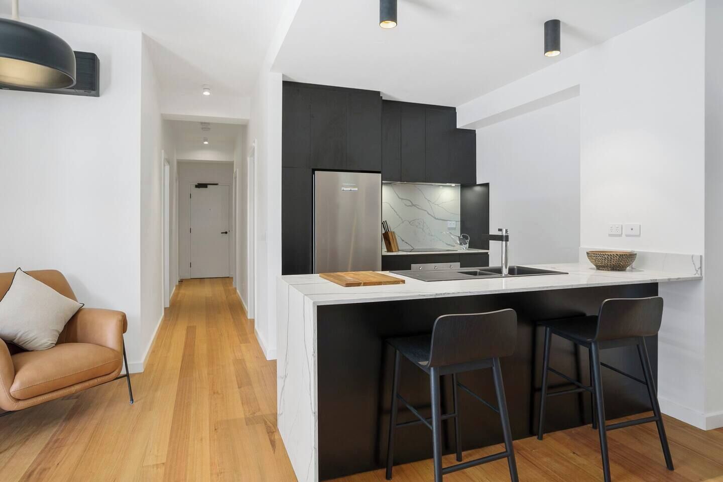 A modern kitchen with a central island, black bar stools, and a white countertop.
