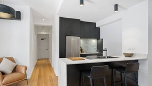 A modern kitchen with a central island, black bar stools, and a white countertop.