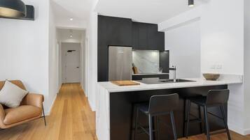 A modern kitchen with a central island, black bar stools, and a white countertop.