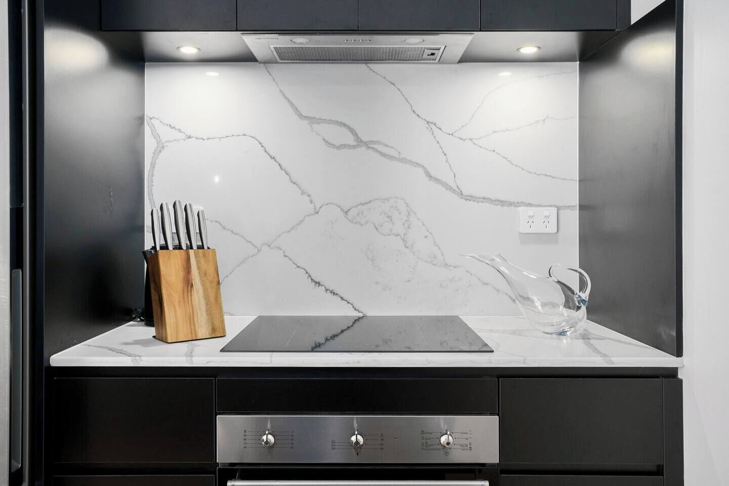 A modern kitchen with a marble backsplash, a wooden knife block, and a stainless steel range hood.