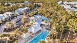 A resort with multiple buildings, a swimming pool, and surrounding palm trees. - "Emerald Bliss" Luxury in NatureWalk 30A | Golf Cart + Bikes + Screened Porch (Santa Rosa Beach)