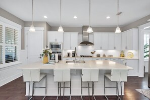 A modern kitchen with white cabinetry, a large island with bar stools, stainless steel appliances, and pendant lighting.