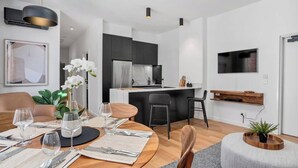 A modern living space with a dining area, kitchen, and a TV mounted on the wall. - Sanctuary at Saddlers Where Rustic Meets Refined (Hobart)