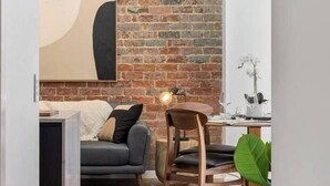 A modern living room with a brick wall, a sofa, a dining table, and a large abstract painting. - Sanctuary at Saddlers Where Rustic Meets Refined (Hobart)
