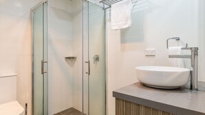 A modern bathroom with a glass shower enclosure, a white sink, and a towel rack.