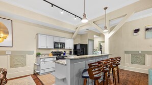 Cucina con mobili bianchi, un'isola centrale con sgabelli da bar, un forno a microonde e un frigorifero.