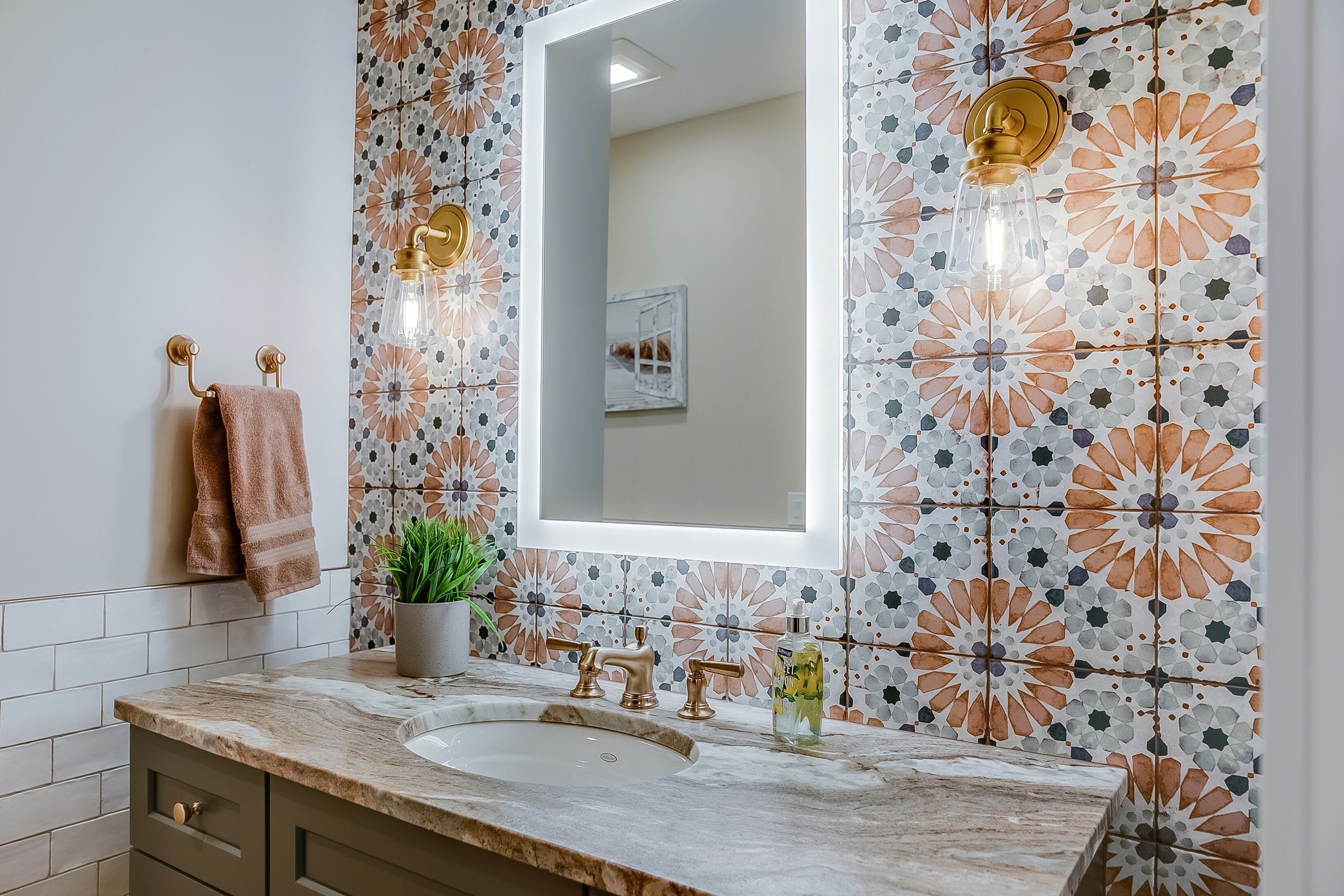 Ein Badezimmer mit Marmorwaschbecken, goldenen Wasserhähnen und einem backsplash mit floralem Muster.