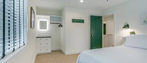Un dormitorio con cama, ventilador de techo, cómoda, espejo, una puerta verde y una ventana con persianas.