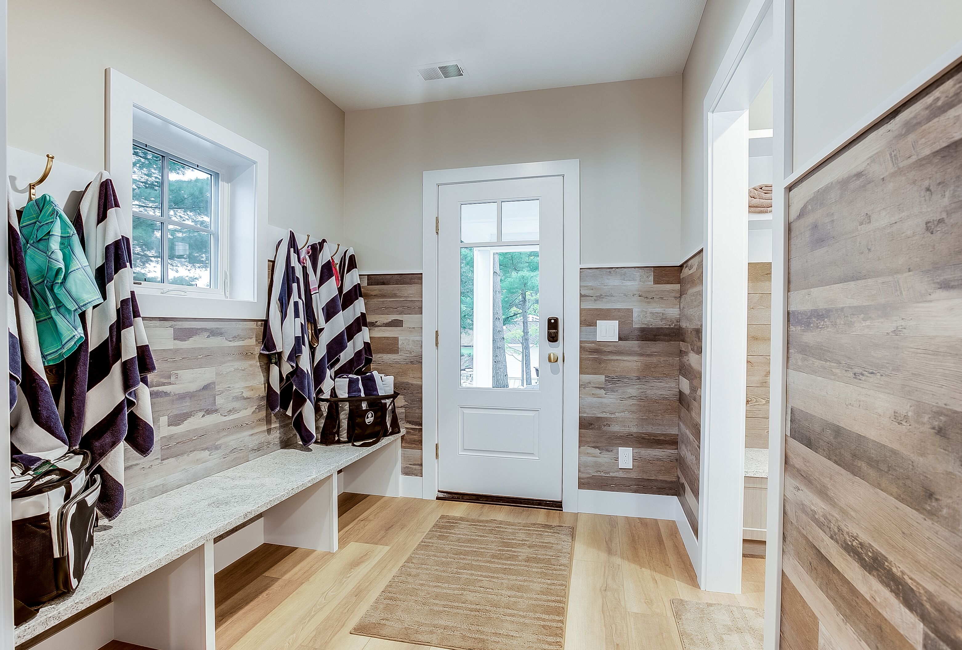A clean, modern bathroom with a bench, towel rack, and a door leading to a wooden interior.