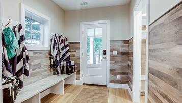 A clean, modern bathroom with a bench, towel rack, and a door leading to a wooden interior.