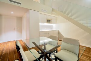 A modern kitchen with a glass dining table, two chairs, and a microwave above the counter.