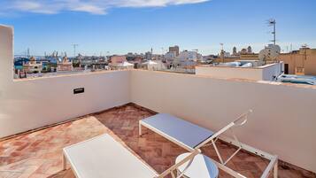 A rooftop terrace with a white table and chair, a herringbone-patterned floor, and a view of the cityscape.