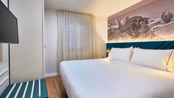 Una habitación de hotel con una cama, televisión, ventana con cortinas y un cuadro de un paisaje urbano en la pared.