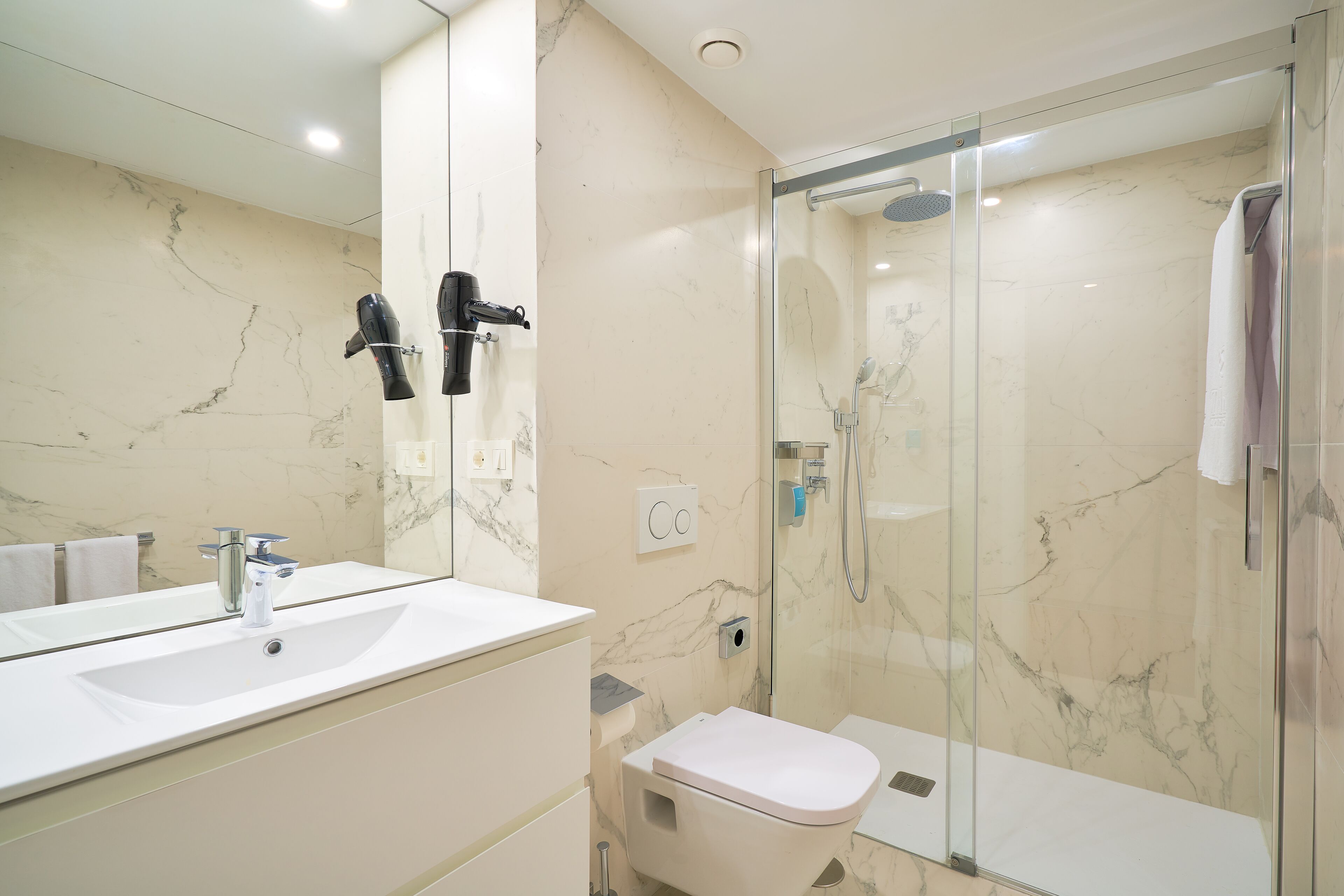 A modern bathroom with a marble sink, a glass-enclosed shower, and a toilet.