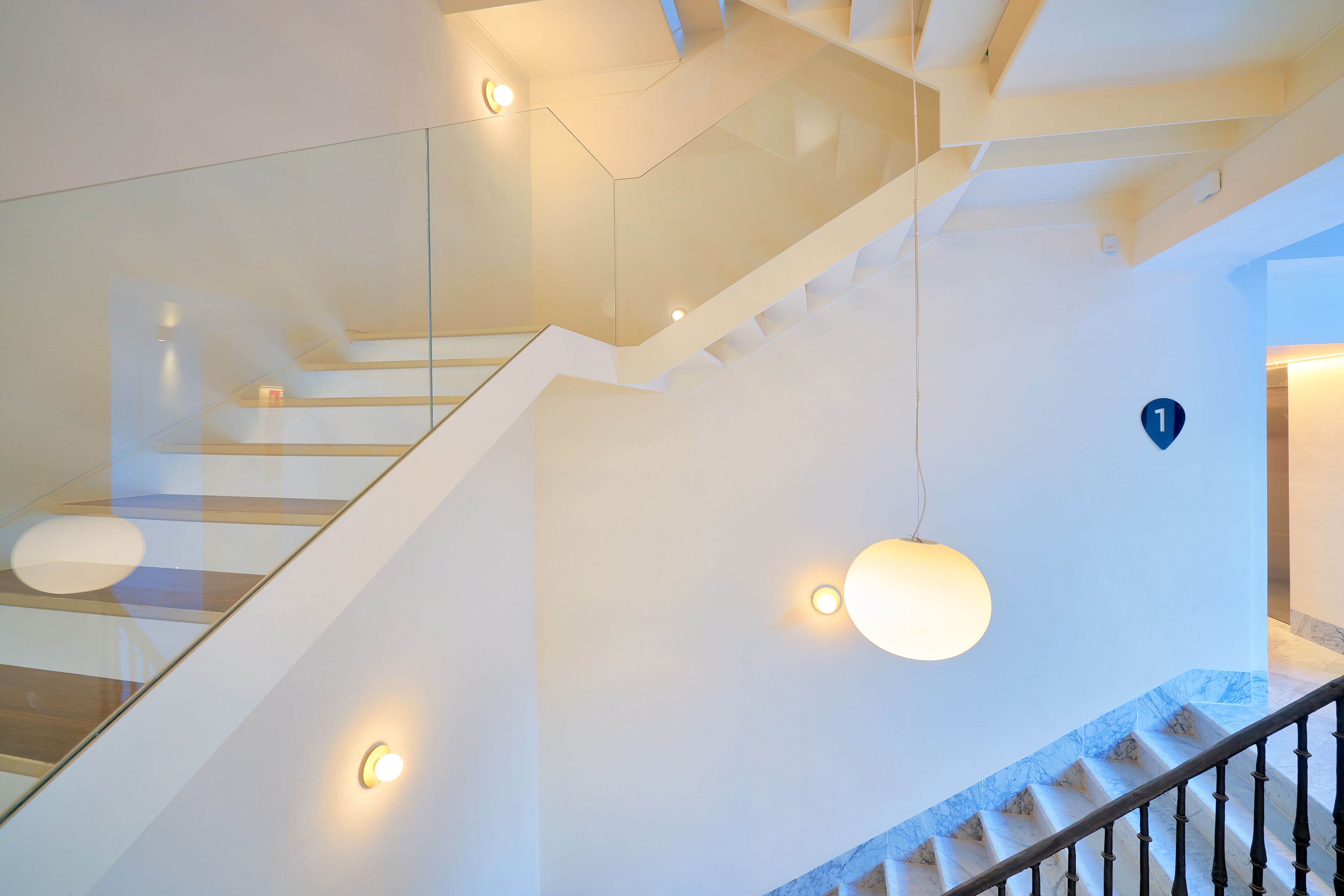 Een moderne trap met glazen balustrades, een marmeren vloer en hanglampen.