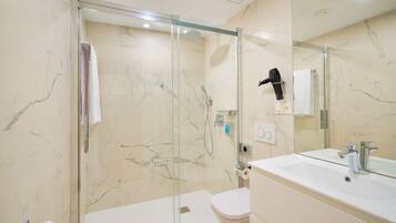 A modern bathroom with a glass-enclosed shower, a white sink, and a toilet.