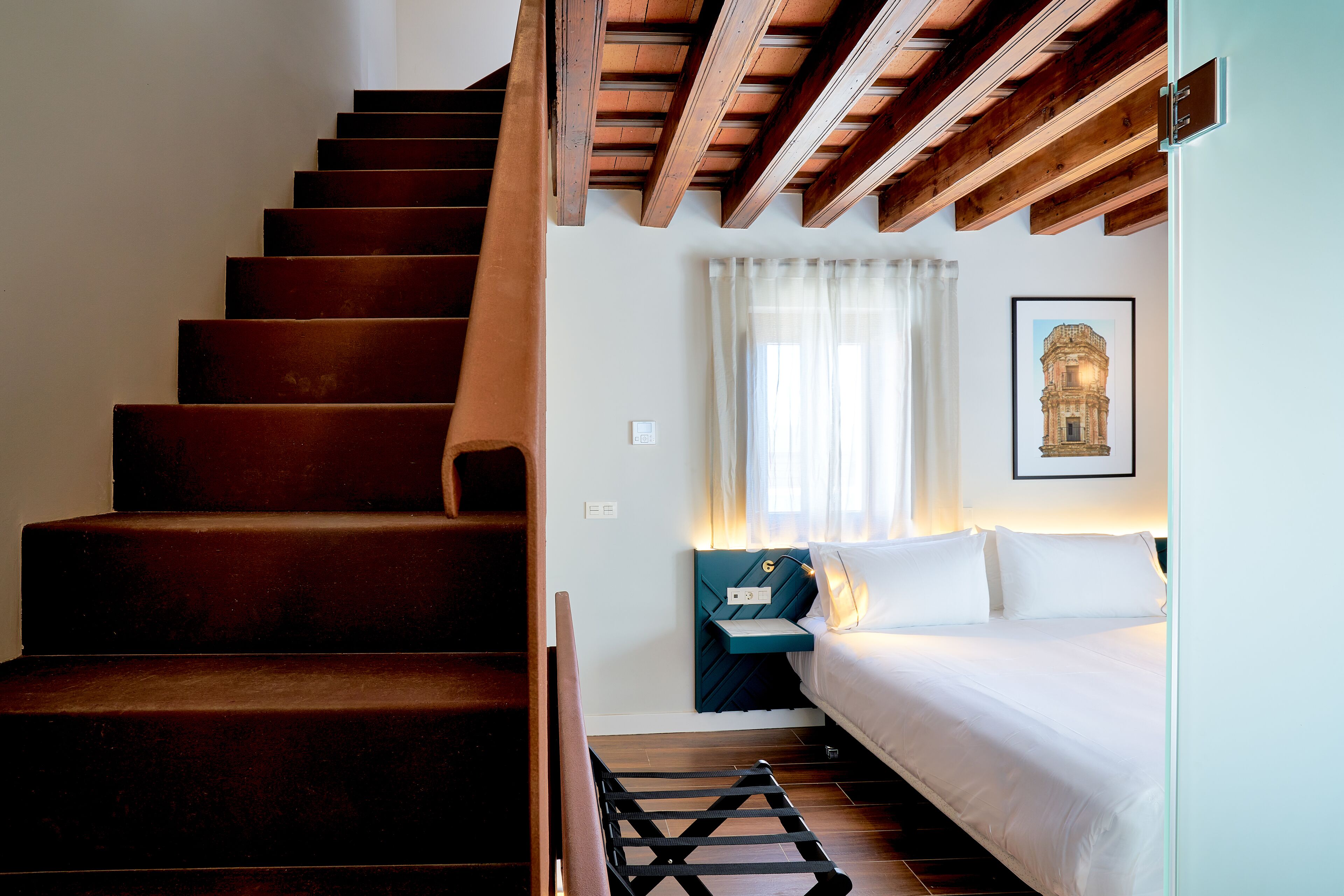 A staircase leading to a bedroom with a bed, a nightstand, and a framed picture on the wall.