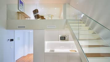 Un interior moderno con una escalera, una zona de cocina con microondas y un área de estar con sillas.