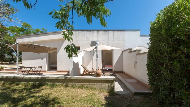 Un patio exterior moderno con suelo de hormigón, dos sombrillas y una mesa con sillas.
