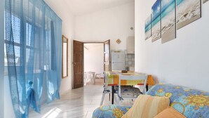 Un dormitorio con cama, una mesa y sillas, un refrigerador y una ventana con cortinas azules.